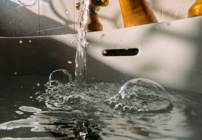 Närbild av vatten som rinner från en kran med bubblor i ett handfat.