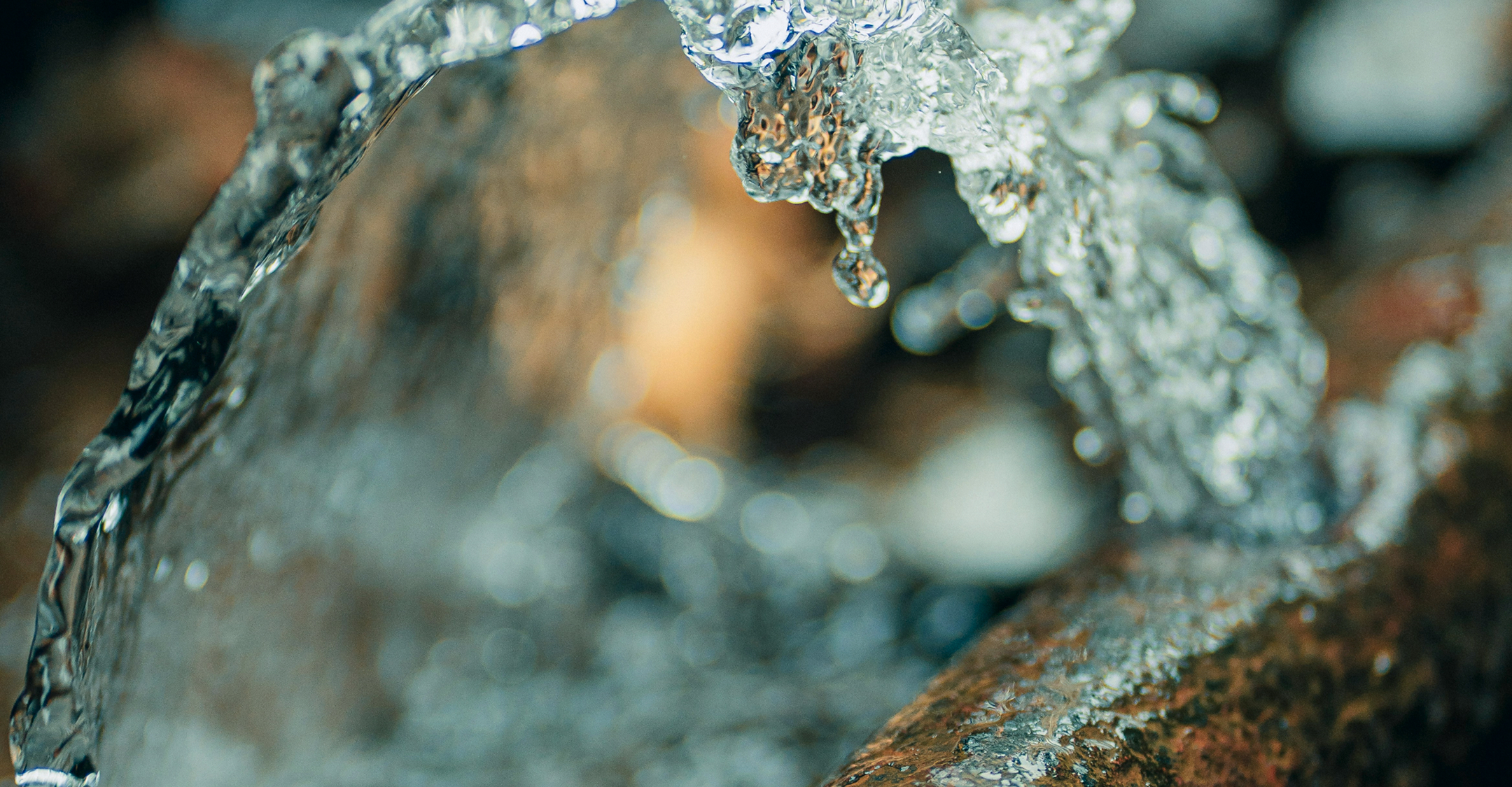 Närbild av rinnande vatten ovanpå en oskarp bakgrund av stenar och jord.