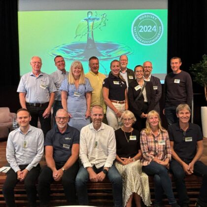 Gruppfoto av glada personer framför en presentation med texten "Nordiskt Vattenskadeseminarium 2024".