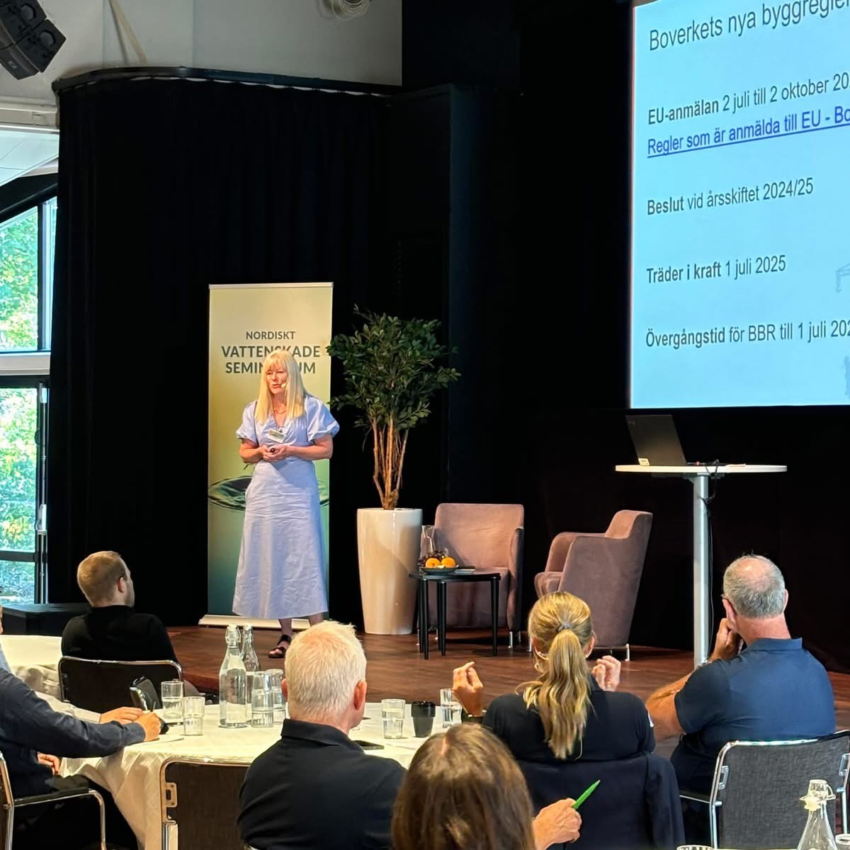 Kvinna håller presentation på scen med bildspel om Boverkets byggregler inför publik på seminarium.