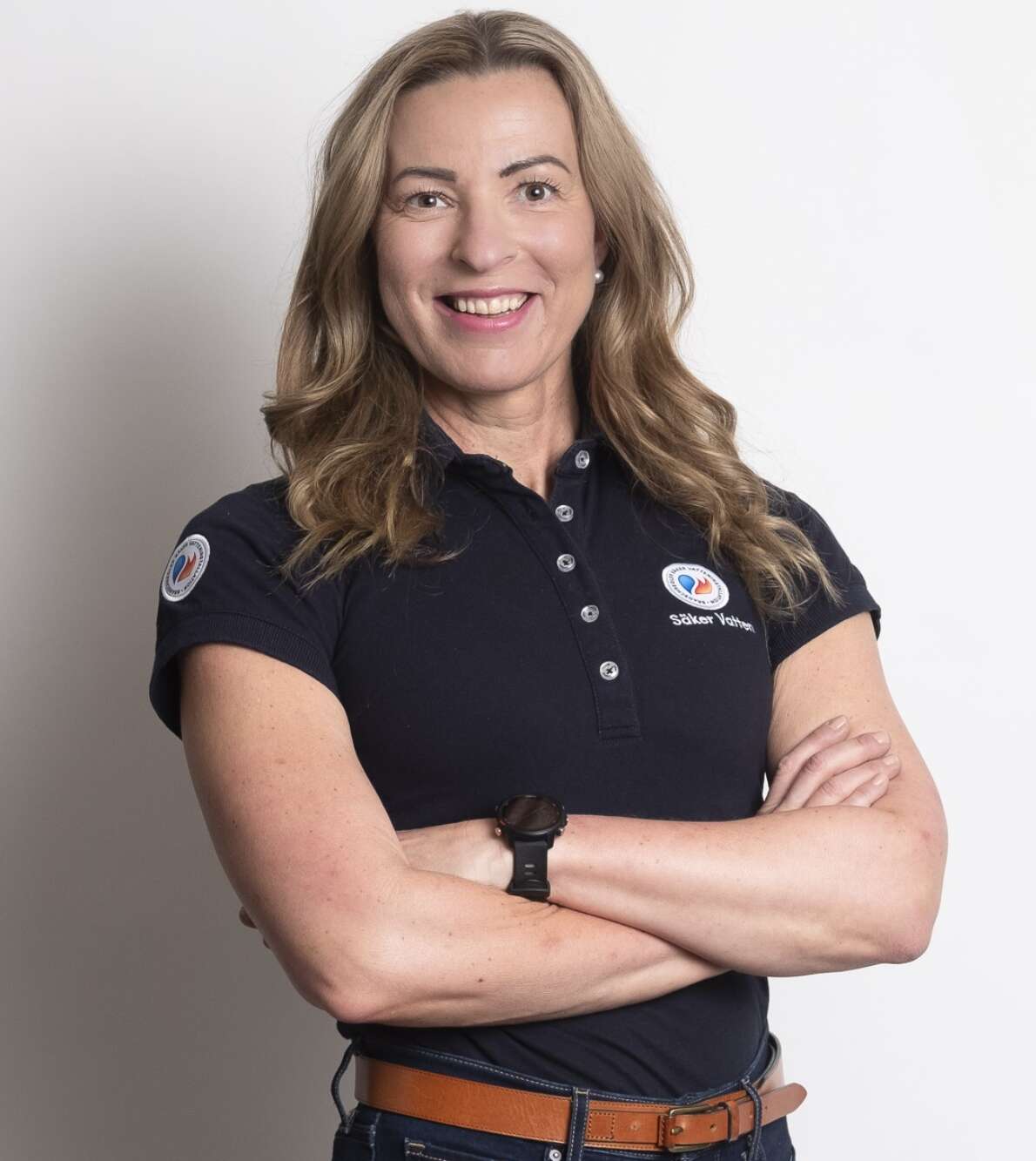 Leende blond kvinna med armarna i kors och blå pikétröja