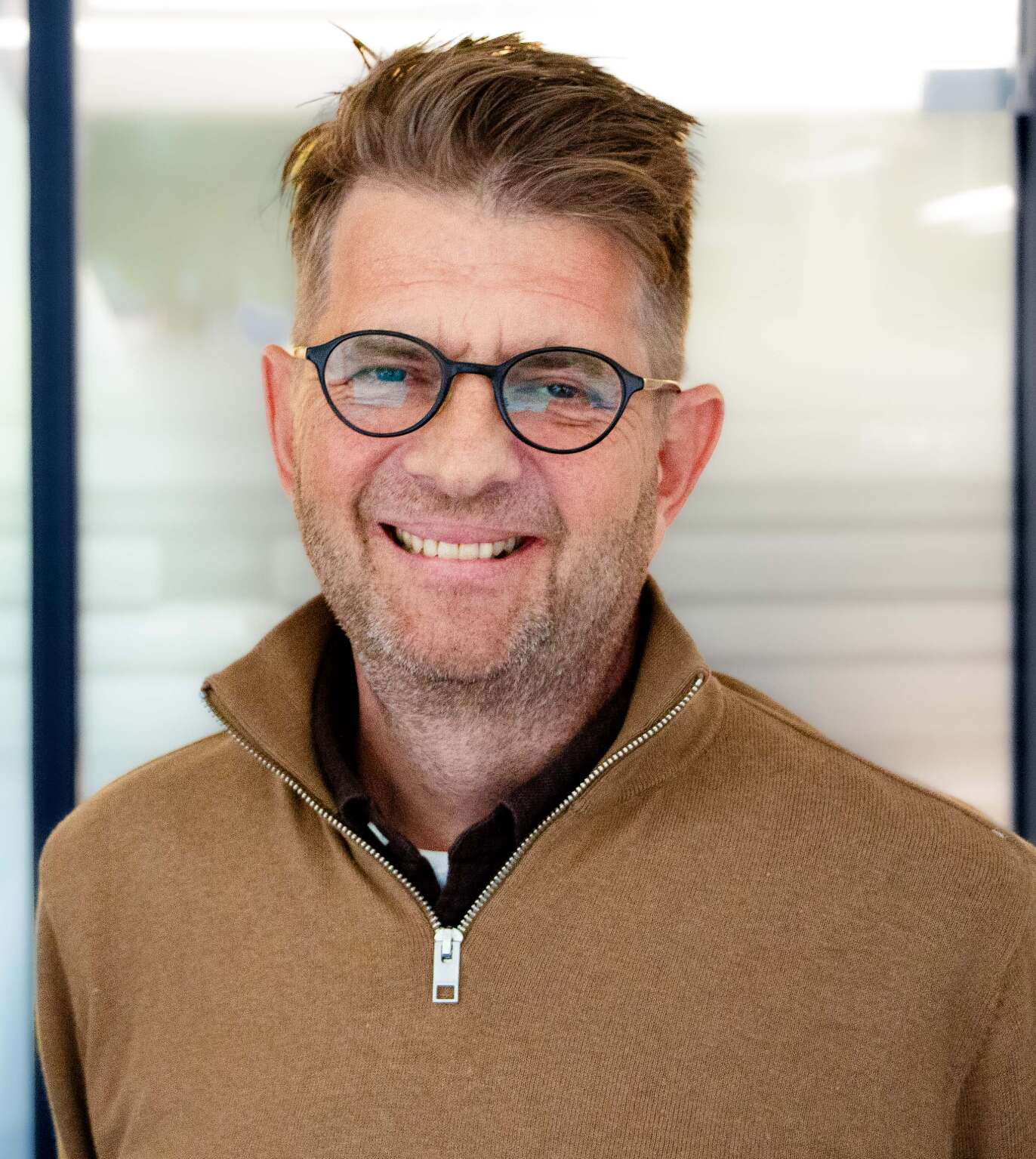 Leende man med glasögon och brun tröja