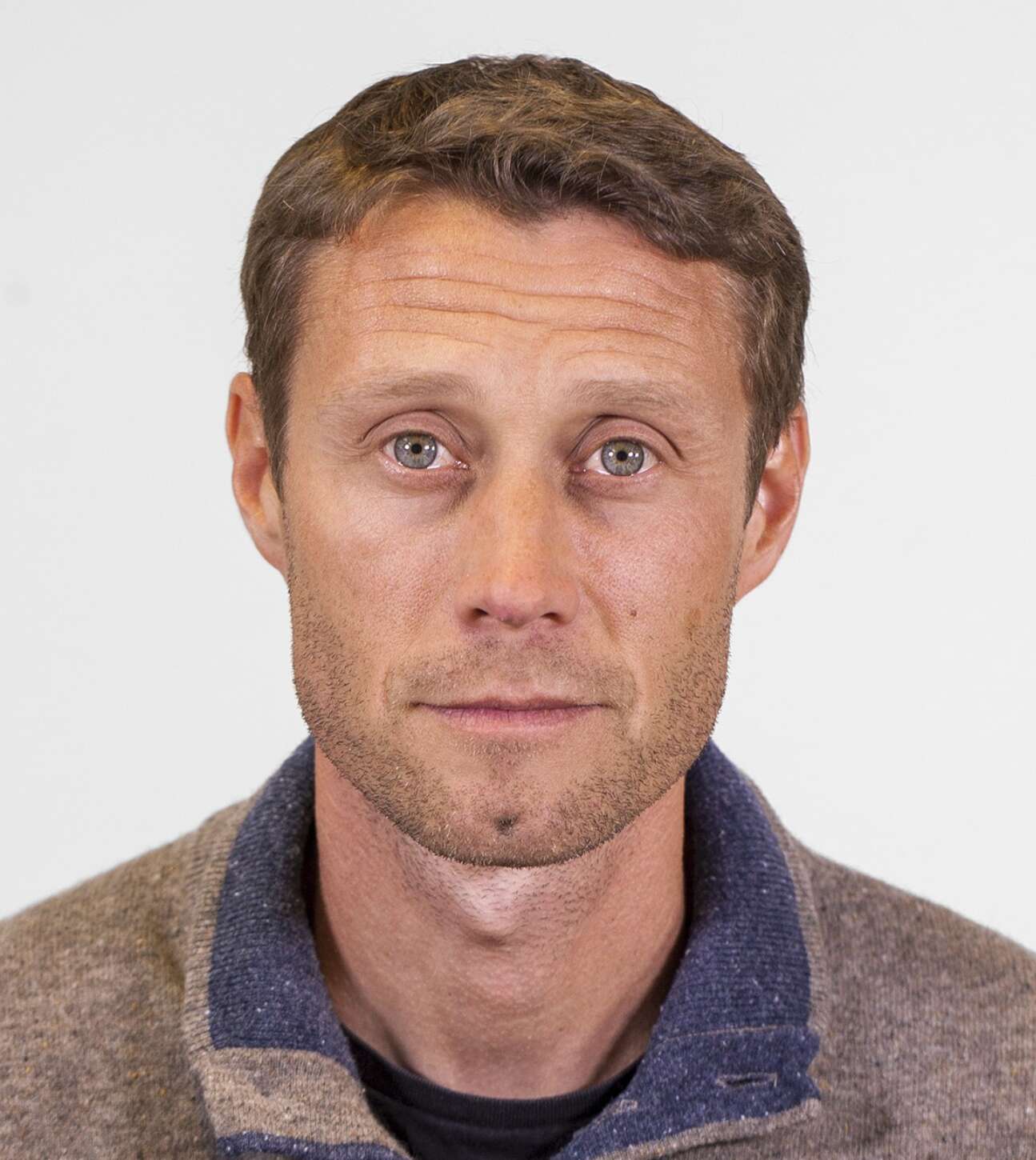 Man med kort brunt hår och skäggstubb