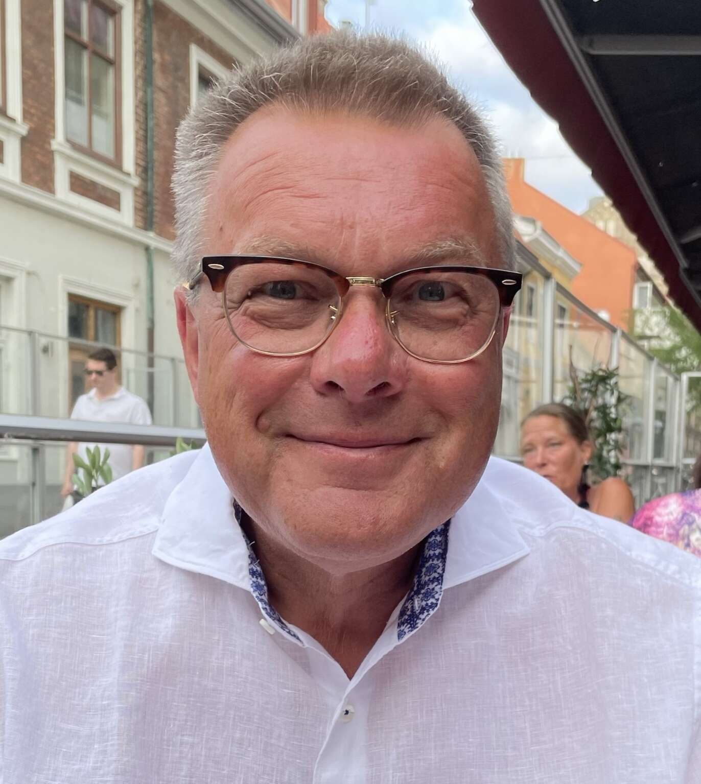 Äldre man med glasögon på ute servering, han har kort hår och en vit skjorta på sig