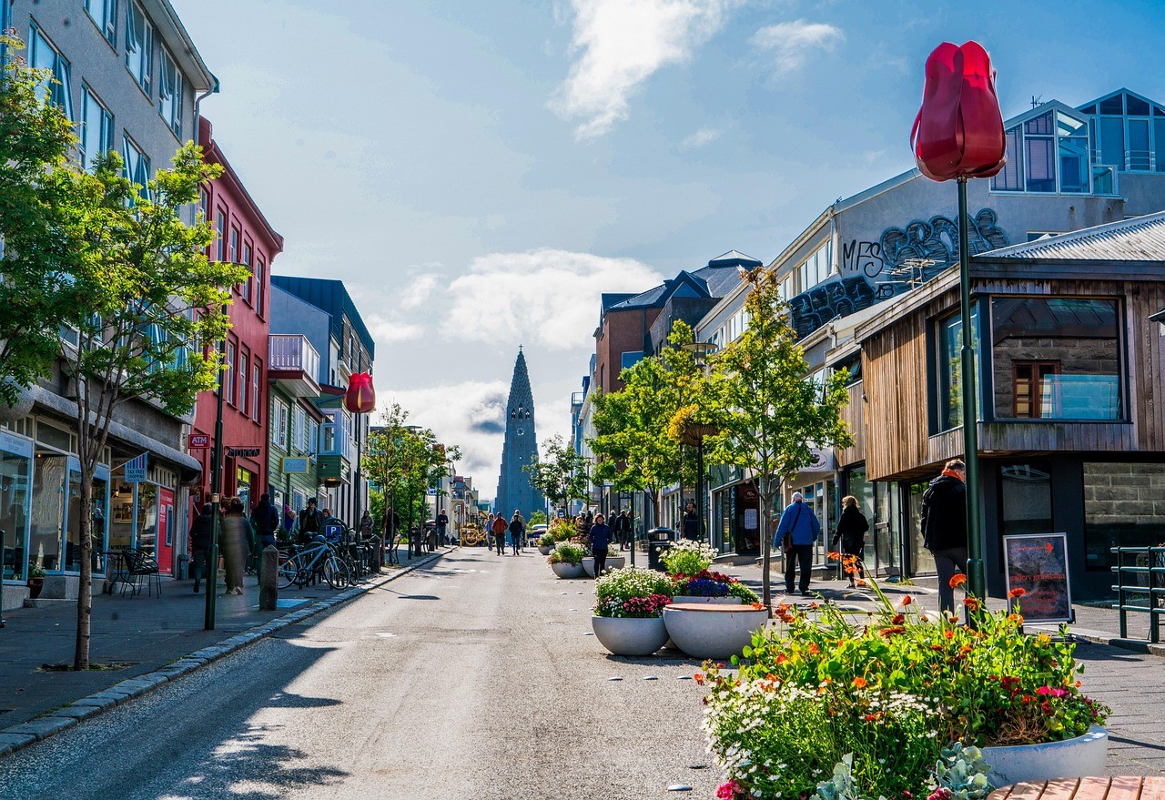 Färgglad stadsgata med blommor, träd, människor och Hallgrímskirkja kyrkan synlig i bakgrunden.